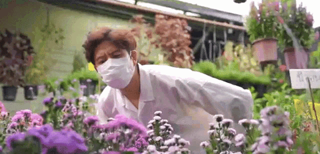 a man wearing a mask is looking at purple flowers .
