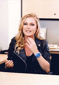 a woman wearing a leather jacket and a blue watch is sitting at a table