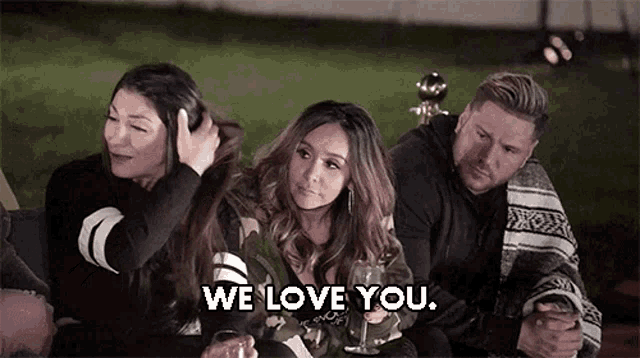 a group of people are sitting on a couch and one of them is holding a glass of wine and saying we love you .