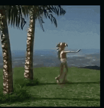 a person in a bikini is walking on a lush green field with palm trees in the background .