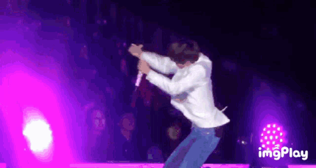 a man in a white shirt is singing into a microphone while dancing on a stage ..