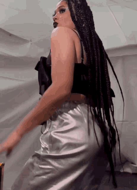 a woman with long braids is wearing a black top and silver pants .