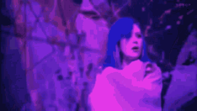 a woman with blue hair and a white shirt is standing in front of a purple background .