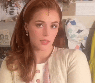 a woman with red hair wearing a headband and a white sweater