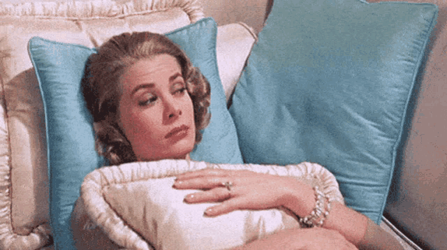 a woman is laying on a couch with blue pillows and a ring on her finger