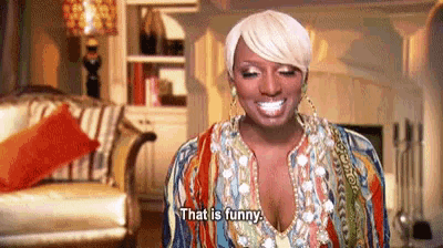 a woman is sitting in a living room with a chair and a fireplace and says `` that is funny '' .