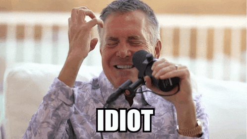 a man laughs while holding a microphone and the word idiot is above him
