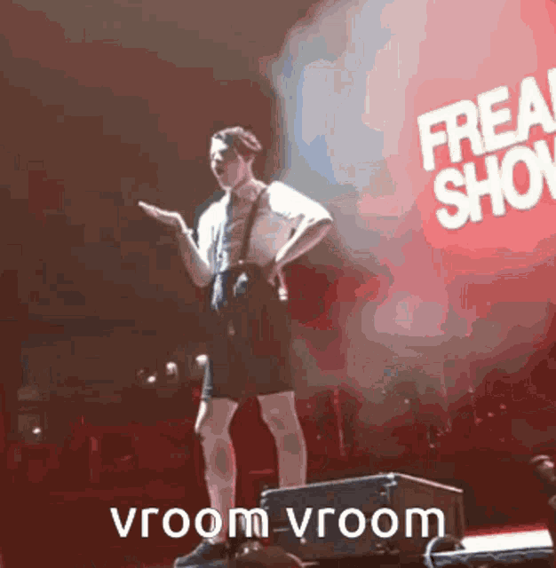 a man stands on a stage in front of a sign that says freak show vroom vroom