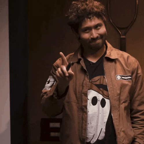 a man wearing a brown jacket and a black shirt with a smiley face on it giving the middle finger