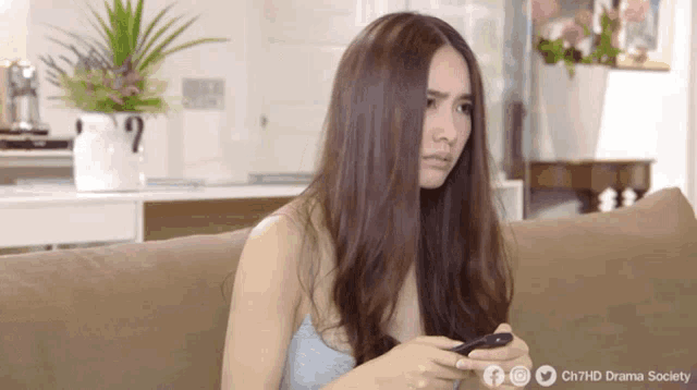 a woman is sitting on a couch looking at her phone with a facebook logo in the corner