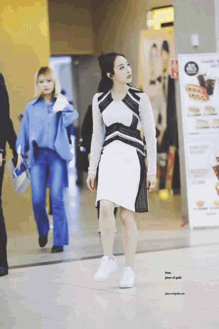 a woman in a white and black dress is standing in front of a sign that says " pieces of gold "