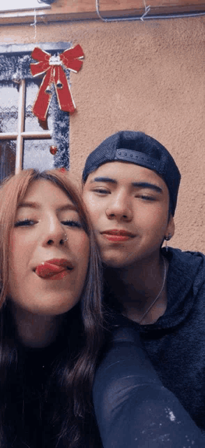 a man and a woman sticking their tongues out in front of a window decorated for christmas