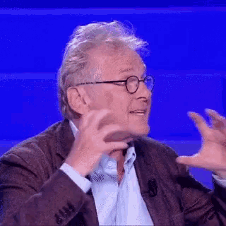 a man in a suit and glasses is making a funny face while talking on a television show .