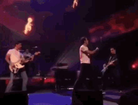 a group of people are playing instruments on a stage in a dark room with red lights .