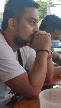a man with a beard is sitting at a table with another man wearing a face mask