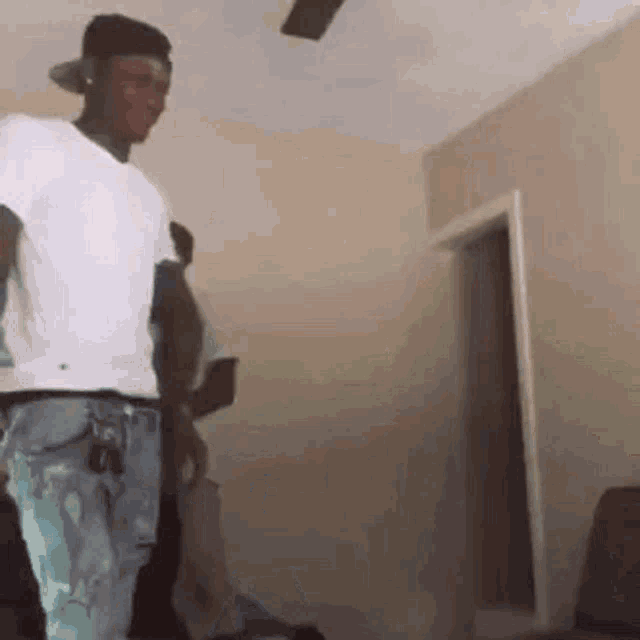 a man in a white shirt and black hat is standing in a living room .