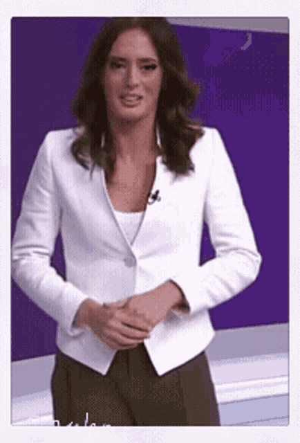 a woman in a white jacket and khaki pants stands in front of a purple wall