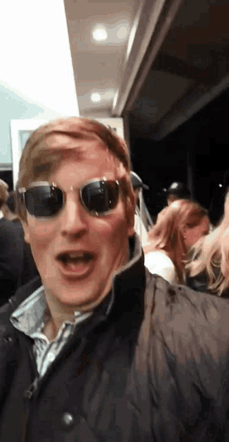 a man wearing sunglasses and a black jacket stands in a crowd