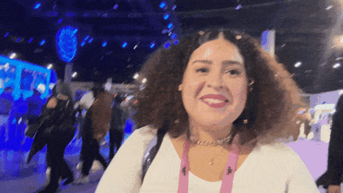 a woman with curly hair wearing a white shirt and a pink lanyard around her neck