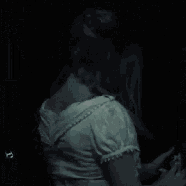 a woman in a white dress is standing in a dark room holding a doll .