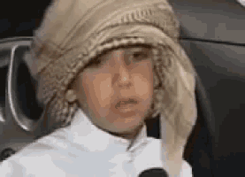 a young boy wearing a turban and a hat is sitting in a car with a microphone .