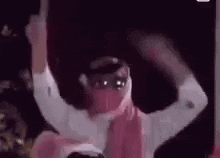a man in a pink scarf is dancing with his arms outstretched in a dark room .