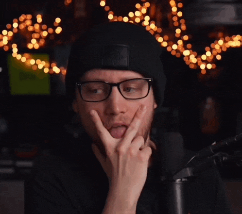 a man wearing glasses and a black beanie sticks his tongue out