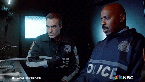 two police officers are standing next to each other in a dark room with a nbc logo in the corner