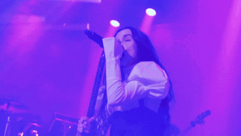 a woman singing into a microphone on a stage with purple lights