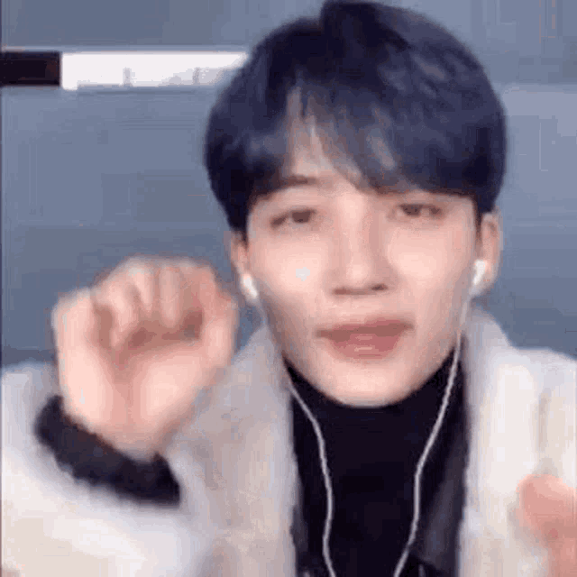 a young man with blue hair and earphones is making a funny face .
