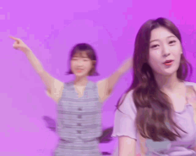 two women are dancing in front of a purple background . one of the women is wearing a striped dress .