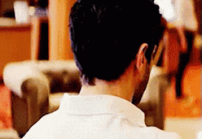 a man in a white shirt is sitting on a couch looking over his shoulder .