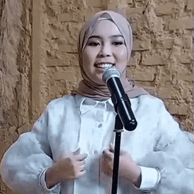 a woman in a hijab is standing in front of a microphone and smiling .
