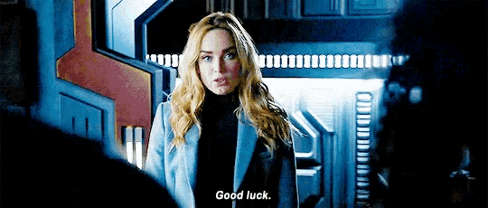 a woman in a blue coat is standing in front of a door and talking to someone .