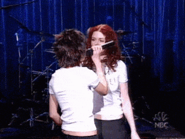 two women are singing into microphones on a stage in front of a blue curtain .
