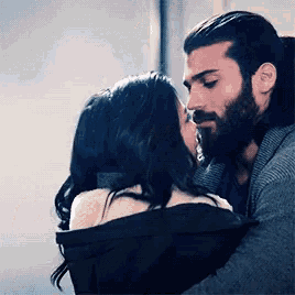a man with a beard and a woman with long hair are hugging and kissing .