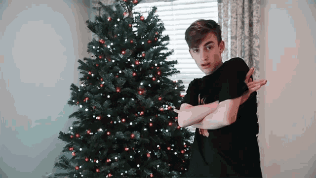 a young man standing in front of a christmas tree wearing a black t-shirt with the letter k on it