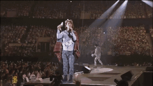 a man singing into a microphone on a stage with a crowd watching