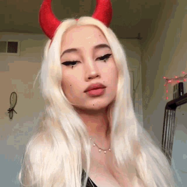 a woman with blonde hair and red horns is wearing a black top and a necklace .
