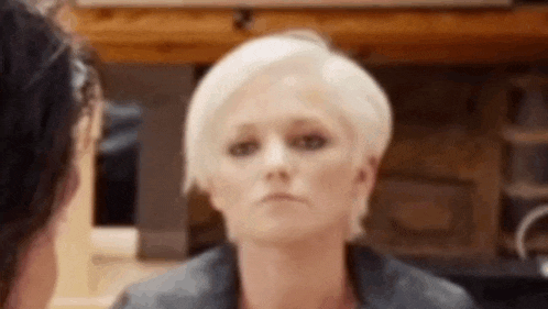 a woman with short blonde hair is making a funny face while sitting at a table .