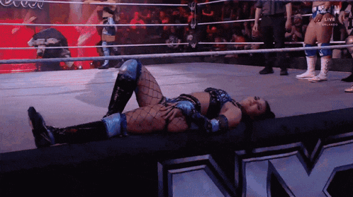 a female wrestler is laying on the floor in a wrestling ring while a referee watches