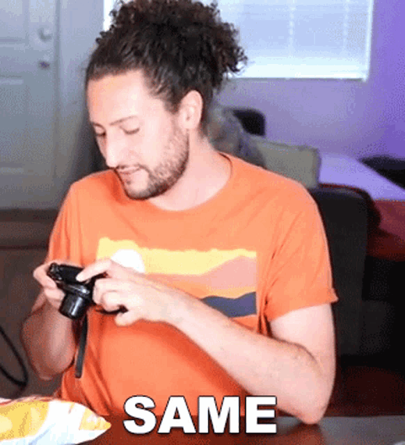a man in an orange shirt is holding a camera and the word same is on the bottom