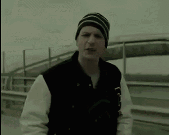 a man wearing a beanie and a varsity jacket is standing on a highway .