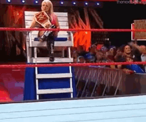 a woman is sitting in a chair in a wrestling ring holding a championship belt