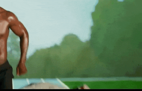 a man without a shirt is running in a field with trees in the background