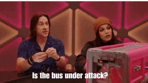 a man and a woman sitting at a table with the words is the bus under attack on the bottom