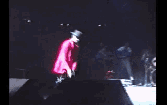 a man in a cowboy hat and a pink shirt is kneeling on a stage .