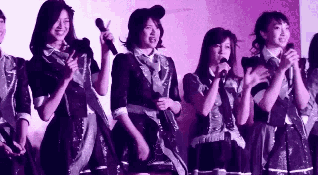 a group of women singing into microphones in front of a purple backdrop