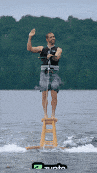 a man is standing on a wooden stool in the water while waving his hand
