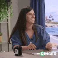 a woman is smiling while sitting at a table with a mug that says r on it